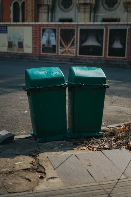 A street scene featuring a white waste collection truck parked alongside a row of historic buildings with diverse architectural styles. The second building from the left is a multi-storey structure co